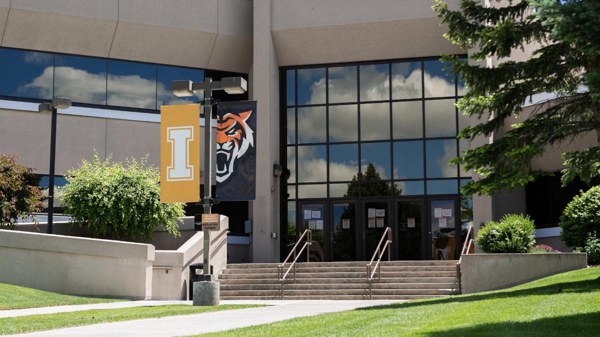 A white block I on a gold banner hangs outdoors on a sunny day at the Idaho Falls campus.