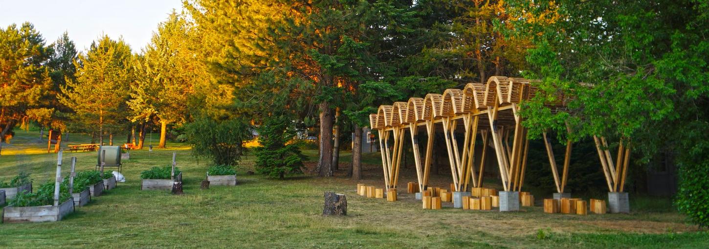 A rolling roof and V-shaped framed outdoor classroom sits before trees.