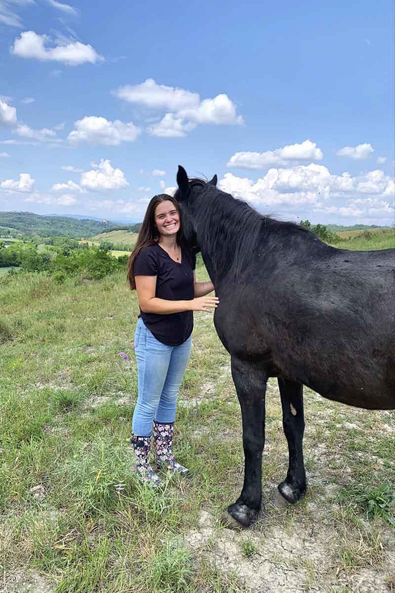 A woman stands next to a horse in a pasture.