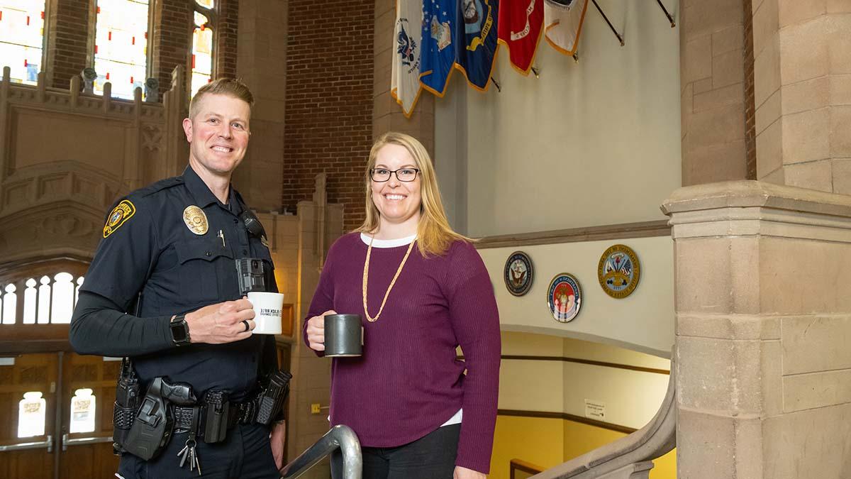 Alumni and Operation Education scholarship recipients Jennifer Tengono and Jason House hold coffee mugs in the lobby of the Memorial Gym