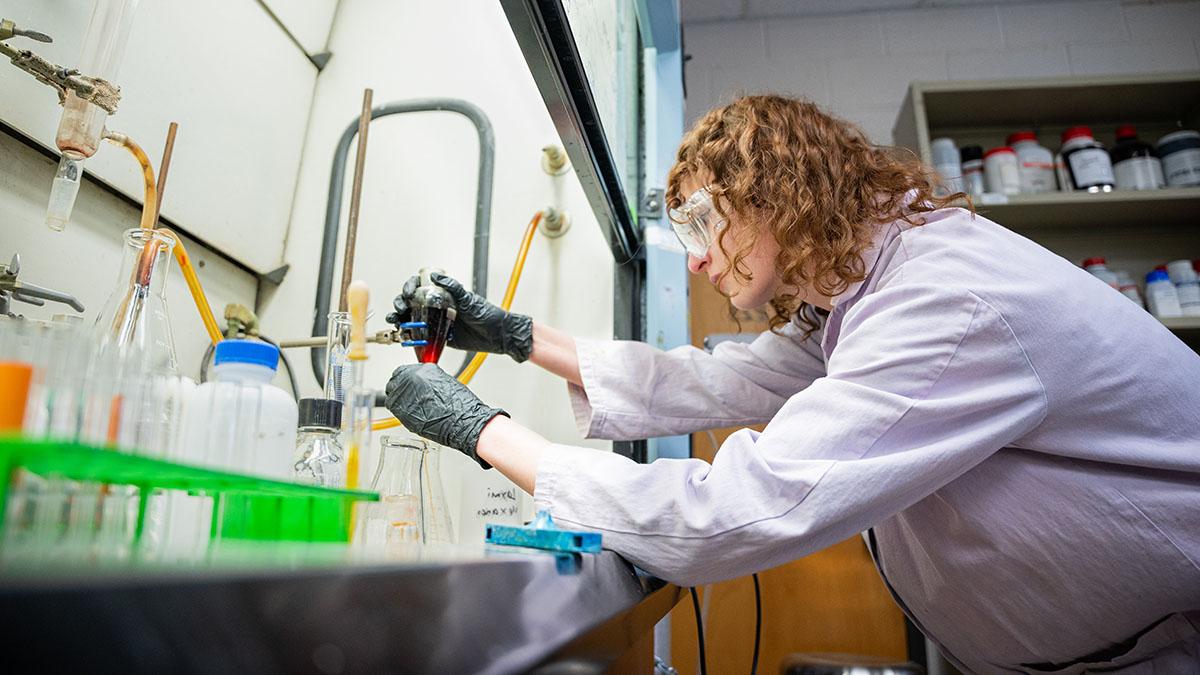 化学实验室里戴着护目镜和实验服的女人正在检查一个烧杯.
